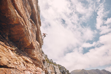 Rock, sport and mountain adventure man climber free climbing rocks in the mountains. Sports person in nature on a outdoor cliff wall experience a freedom lifestyle and healthy strength challenge