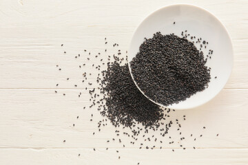 Bowl of black sesame seeds on light wooden background