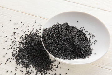 Bowl of black sesame seeds on light wooden background, closeup