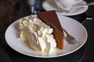 Piece of famous Sachertorte chocolate cake with apricot jam of Austrian origin served with whipped cream