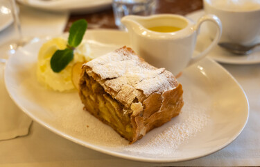 Austrian sweet dessert, portion of apple strudel with whippen cream and hot vanilla sauce served in old bakery cafe in Vienna, Austria
