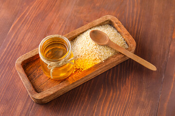 Board with jar of oil and sesame seeds on wooden background