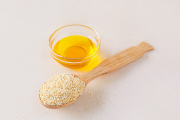 Spoon with sesame seeds and bowl of oil on light background