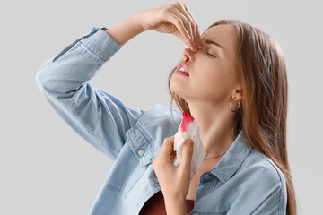 Young woman with nosebleed and tissue on light background, closeup