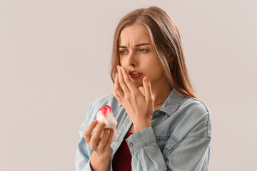 Young woman with nosebleed and tissue on light background