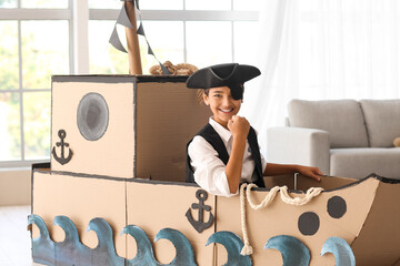 Little boy dressed as pirate playing in cardboard ship at home