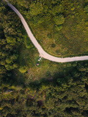 Top down aerial drone view of the road in mountain range trough the trees and forest and car parked wild travel rural vacation and nature concept background