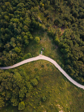 Top down aerial drone view of the road in mountain range trough the trees and forest and car parked wild travel rural vacation and nature concept background