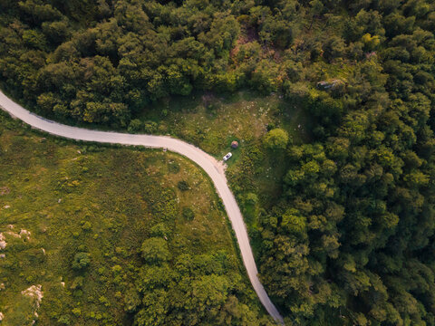 Top down aerial drone view of the road in mountain range trough the trees and forest and car parked wild travel rural vacation and nature concept background