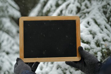 Winter frame for the inscription.copy space.Winter mockup. Chalk empty board in hands on winter snowy forest background.Winter season.