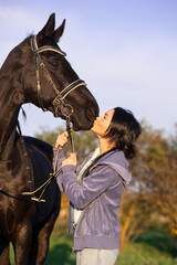 Obraz premium woman kissing her beautiful black horse in green grass meadow. spring time