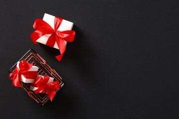 Shopping basket and white gift boxes with red ribbon bows on black background. Black Friday...