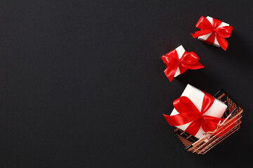 Shopping basket and white gift boxes with red ribbon bows on black background. Black Friday Sale banner template. Top view with copy space.