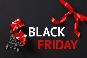 Black Friday banner design. Shopping card, gift boxes, red ribbon bow on black background.