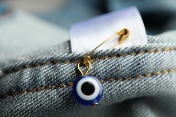 Evil eye safety pin on denim clothing, closeup