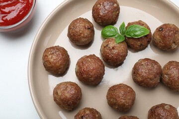 Tasty cooked meatballs with basil on white table, flat lay
