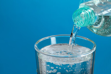 Pouring soda water from bottle into glass on light blue background, closeup. Space for text