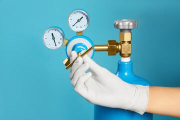 Medical worker checking oxygen tank on light blue background, closeup