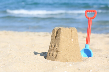 Beautiful sand castle and plastic shovel on beach near sea, space for text