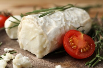 Delicious goat cheese with tomato and rosemary on wooden board, closeup