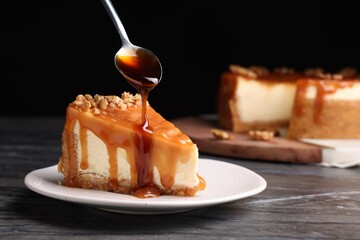 Pouring caramel sauce onto delicious piece of cheesecake with walnuts on black marble table, space...