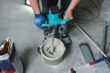 Professional worker mixing plaster in bucket indoors, closeup - obrazy, fototapety, plakaty