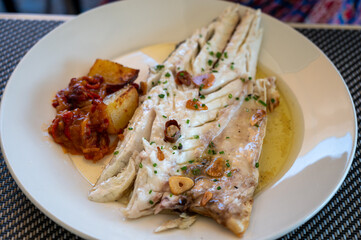 Eating in restaurant of fresh grilled on old charcoal parrillas sea bass fish in small fisherman's village Getaria, Basque Country, Spain