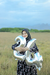 A smiling beautiful girl in a flowery black dress holds the number 24 of balloons for her birthday. Indonesian Woman