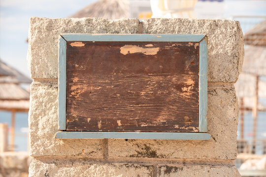 Sign with space for text at entrance to beach, cafe. Brown shabby wooden board without inscriptions. Empty table on stone fence in beach area. Announcement for tourists, menu, advertising, signboard