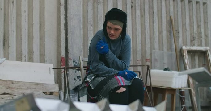 Sick Caucasian homeless woman with itchy skin scratching in slow motion sitting on city street. Portrait of helpless young poor beggar with symptoms of dermatographia outdoors. Cinema 4k ProRes HQ