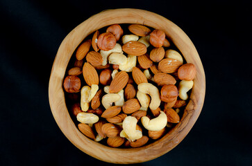 Nuts in assortment in wooden dishes on a black background close-up from above.