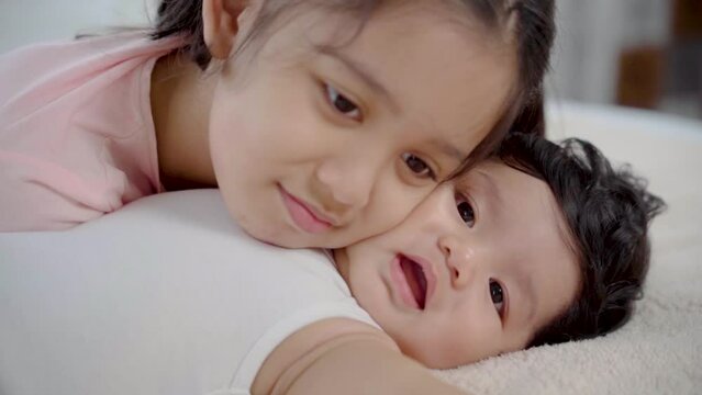 Slow motion of Elder sister kissing newborn baby while lying on bed, adorable girl kiss cheeks toddler with love and care. cute little girl play with brother after him wake up. Family and Healthy.
