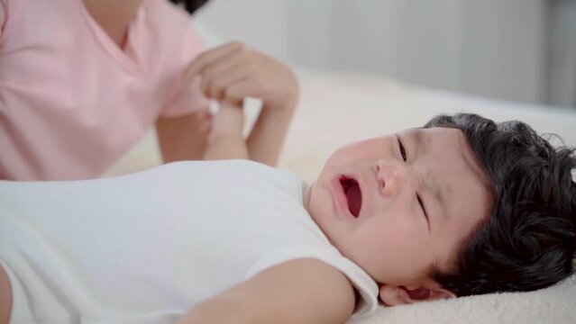 Asian newborn crying lying down on bed with elder sister, infant feel uncomfortable or hungry, adorable girl take care toddler 1-2 month while mother prepare milk for child, sibling playing together
