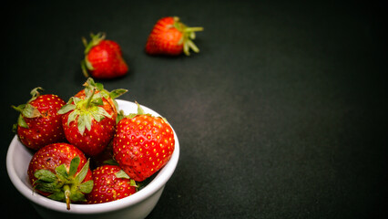 Fresh ripe delicious strawberries in a white bowl on a black background
