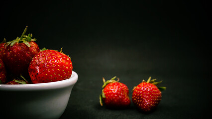 Fresh ripe delicious strawberries in a white bowl on a black background