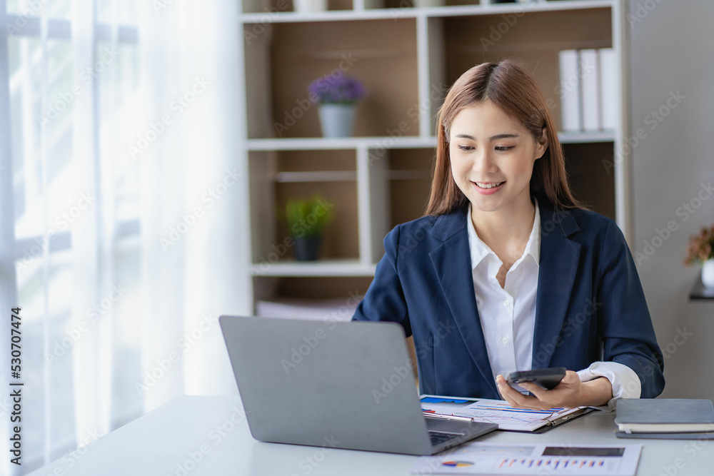 Wall mural Adorable Asian businesswoman enjoying success working in the office with her laptop and company financial accounting documents.