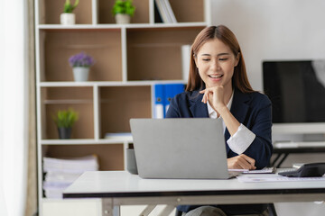Adorable Asian businesswoman enjoying success working in the office with her laptop and company financial accounting documents.