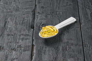 A plastic spoon filled with fish oil capsules on a wooden table.
