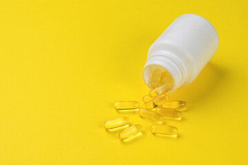 Fish oil capsules spilling out of a white jar on a yellow background.