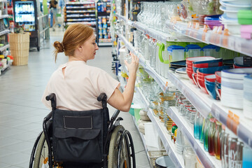 Obraz premium back view of a woman choosing goods in a supermarket, sitting in a wheelchair