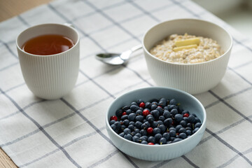 Healthy food breakfast with oatmeal porridge in bowl with summer berries - cowberry, blueberry, slice of butter, herbal tea. Clean eating, dieting, weight loss concept. Shallow depth of field