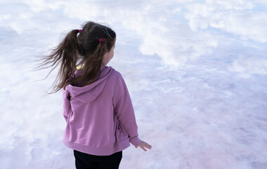 Bursol pink lake. A girl with ponytails stands on the shore of a salt lake and looks into the distance. Clouds are reflected in pink water. Concept: freedom, looking into the bright future, lightness