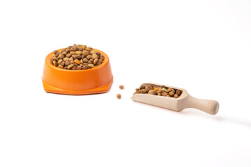 A bowl full of dry pet food, and a scoop full of food on a white background.