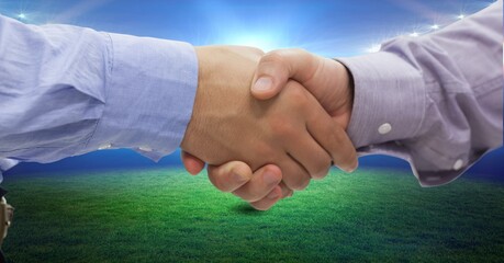 Composition of two businessmen shaking hands over sports stadium