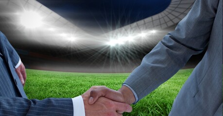 Composition of two businessmen shaking hands over sports stadium