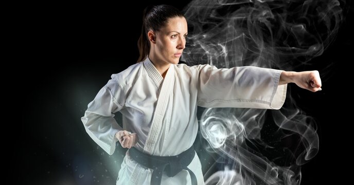 Composition of female martial artist over trails of smoke on black background