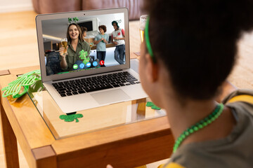 Mixed race woman at home having st patrick's day video call with female friend at bar on laptop