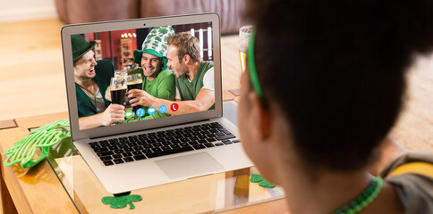 Mixed race woman having st patrick's day video call with happy male friends on laptop at home - Powered by Adobe