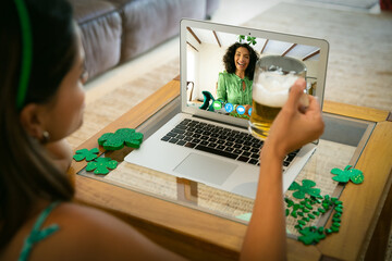 Caucasian woman holding beer having st patrick's day video call with friend on laptop at home