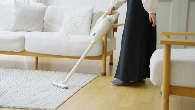 部屋でハンディ掃除機をかけるシニア女性（掃除・家事）